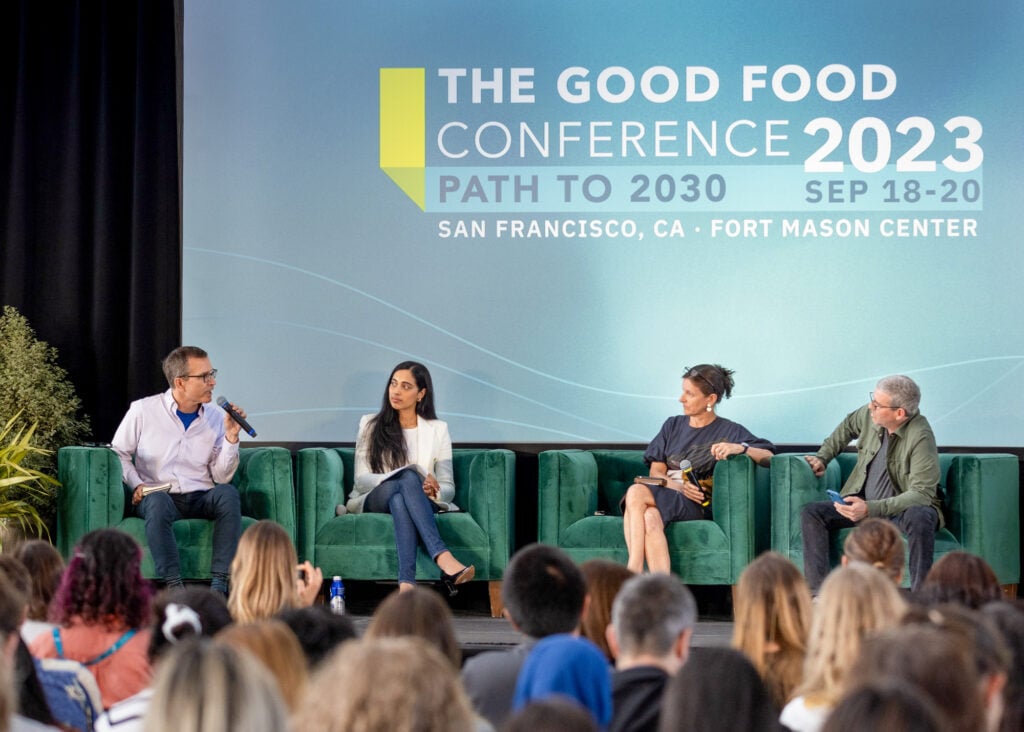Year in review 2023 64 Four people sit in green arm chairs on the good food conference stage in front of a crowd. Bruce friedrich, left, speaks into a microphone.