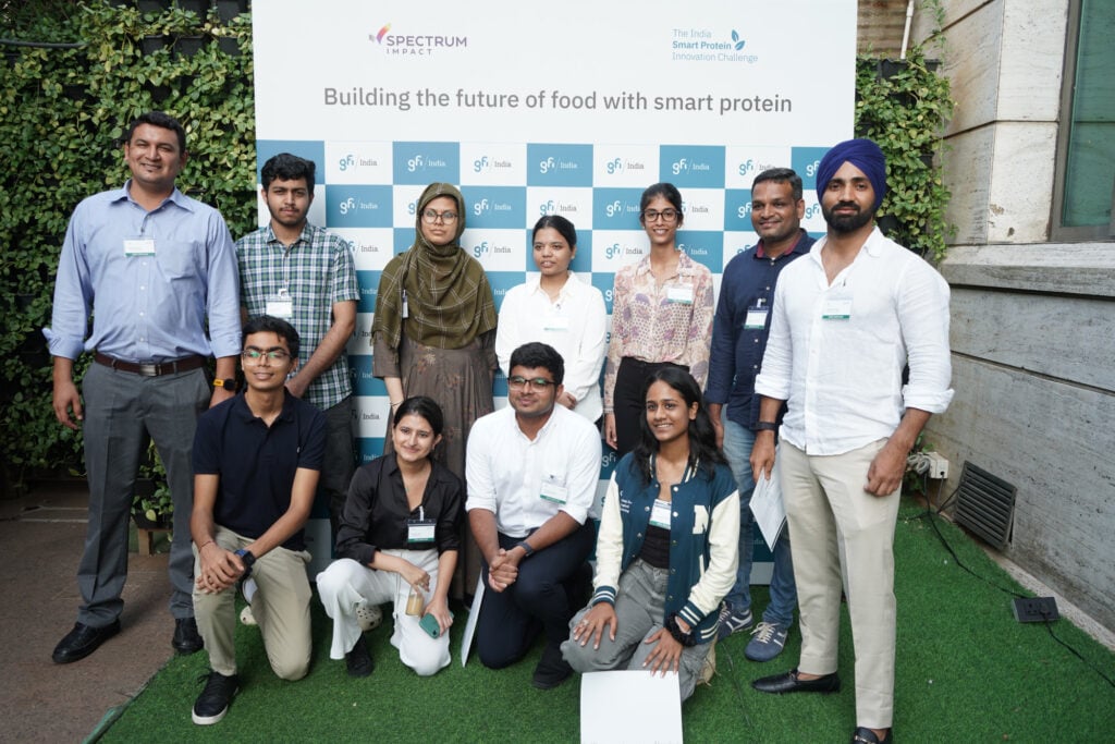 A group of eleven challenge participants stand in front of a white backdrop that says “building the future of food with smart protein”